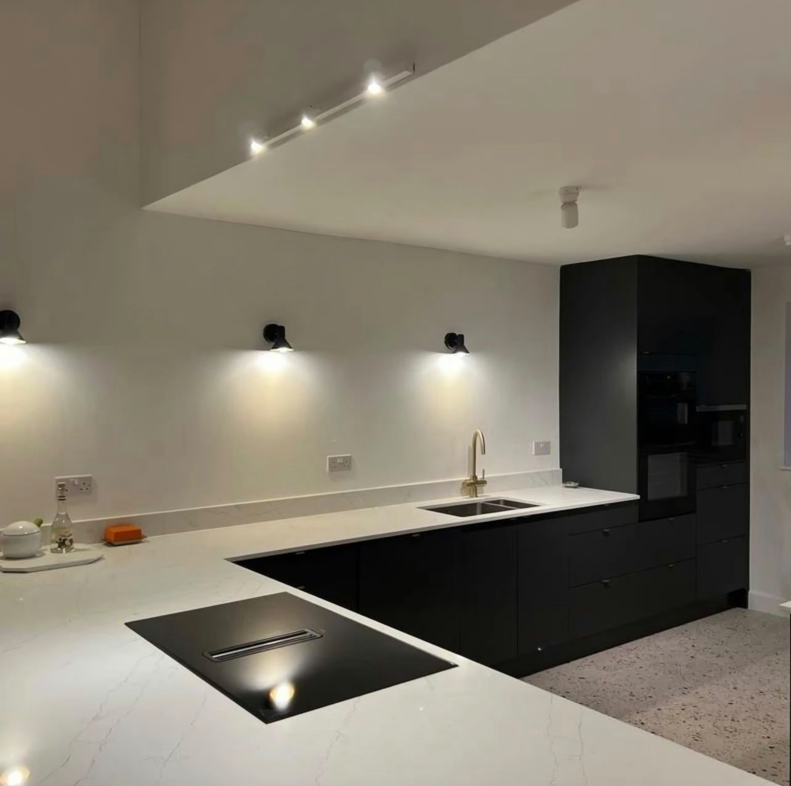 Alaska worktop turning the corner past a flush induction hob to the sink, under a run of black wall lights