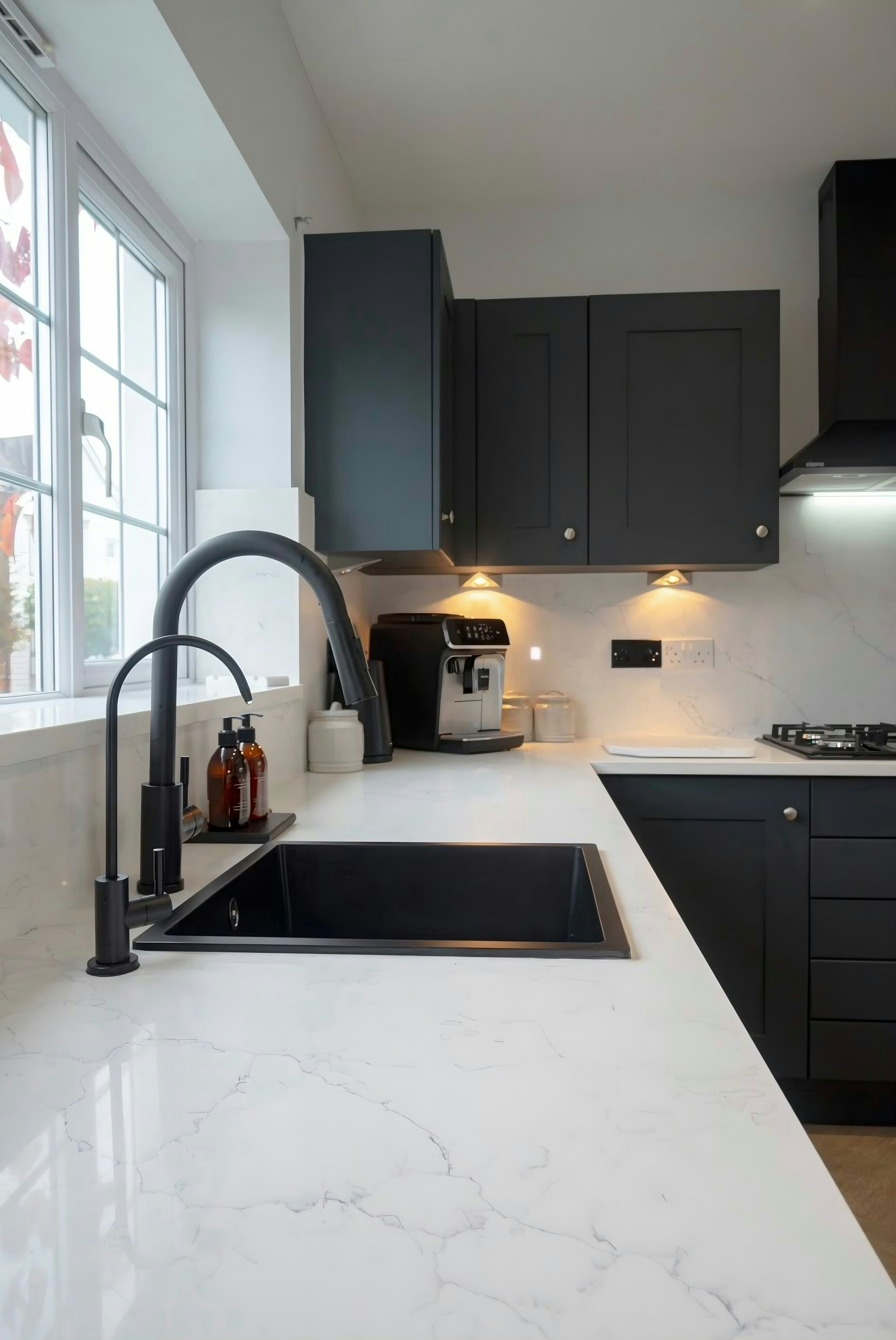 Black undermount sink and pull-down tap in an Alaska worktop by the window, the run carrying on to the hob