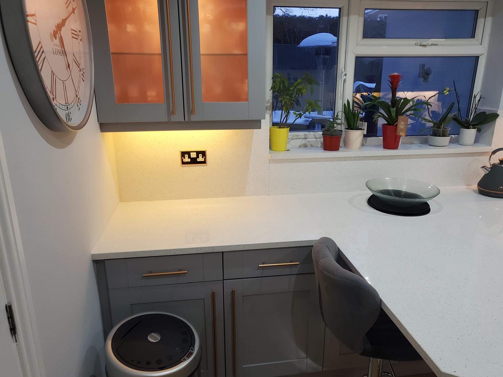 Arctic Starburst worktop turning into the window run, with potted herbs on the sill above it