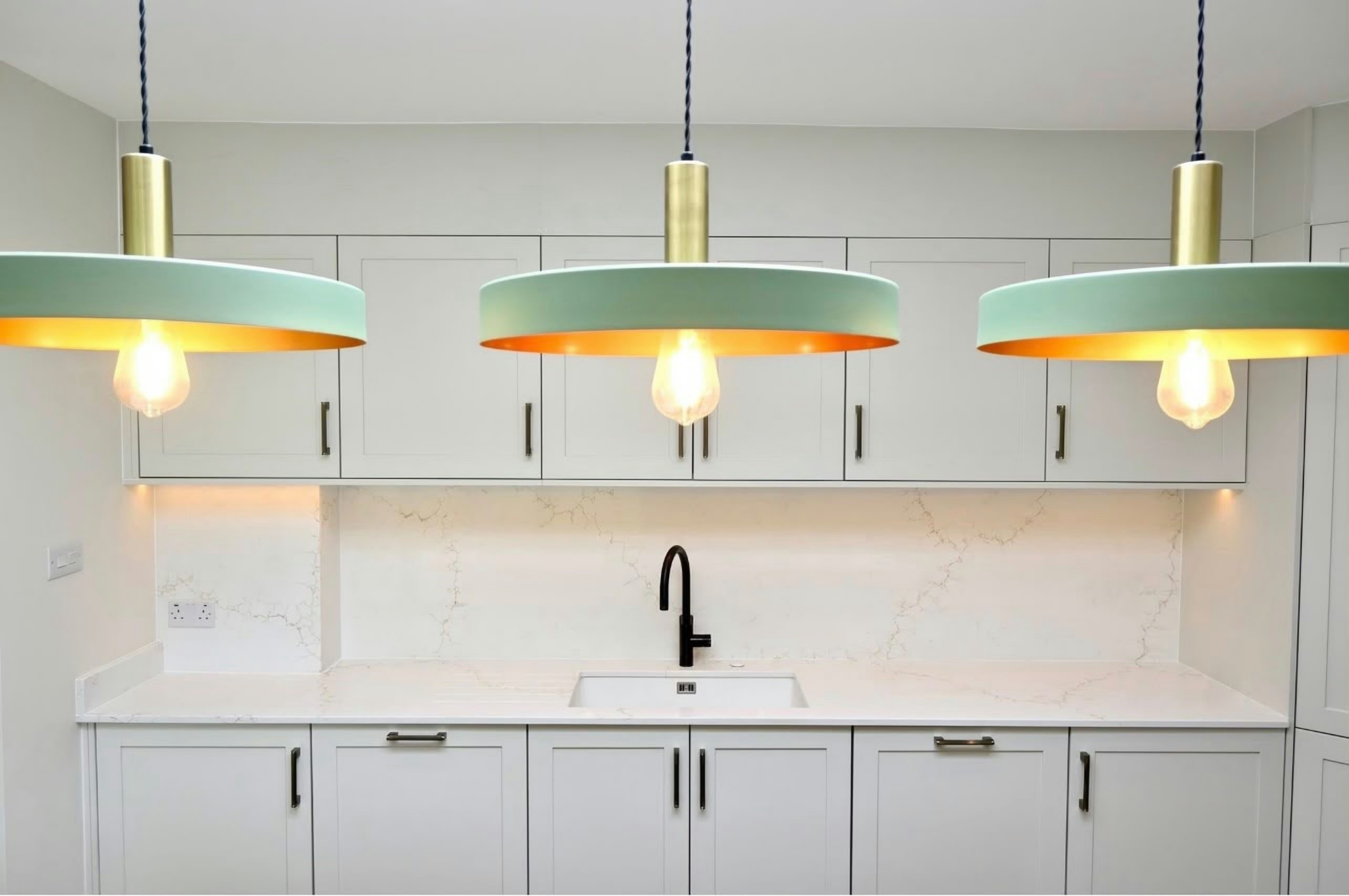 Aurora Gold full-width splashback, run between white shaker wall and base units with three mint and copper pendants hanging in front