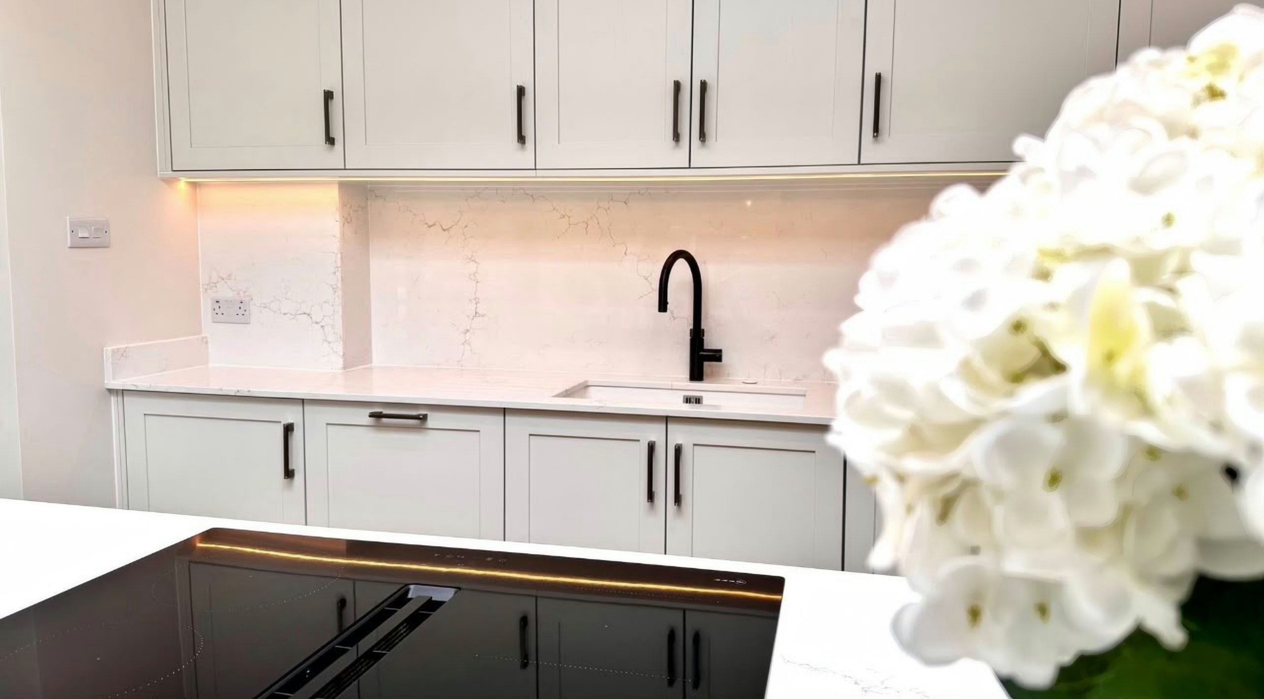 Aurora Gold splashback and worktop behind the sink, seen across the island hob with white hydrangeas in the foreground