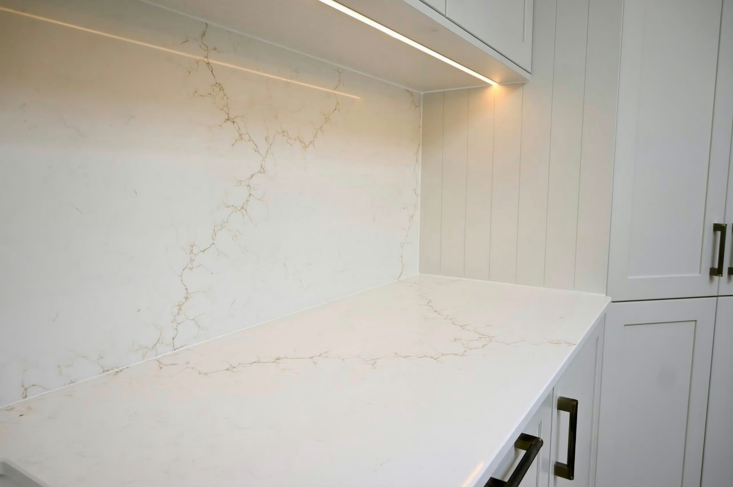 Aurora Gold worktop meeting its splashback in the corner beside a tall housing, lit by an LED strip under the wall units