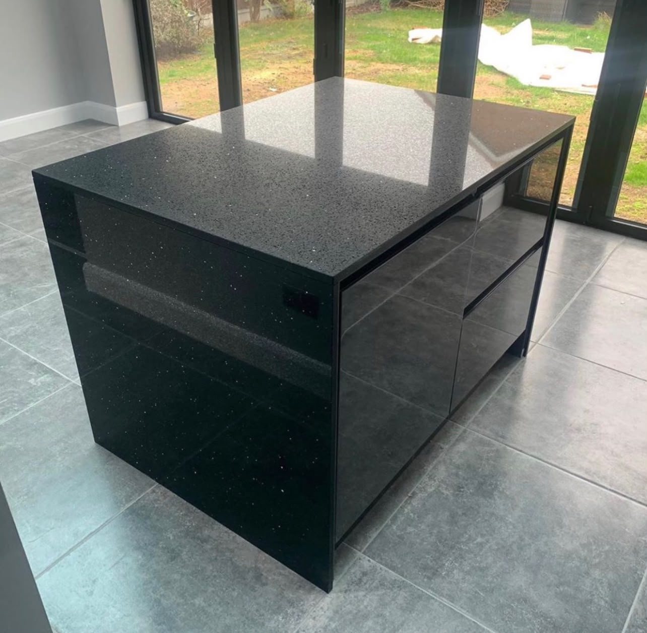 Black Sparkle quartz island with mitred sides, on a grey porcelain floor in front of garden doors