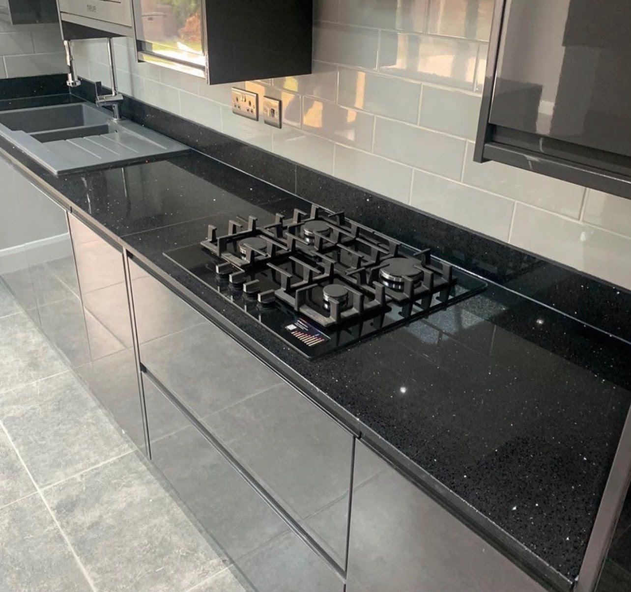 Gas hob in a Black Sparkle run below a metro tile splashback, with the sink and drainer beyond