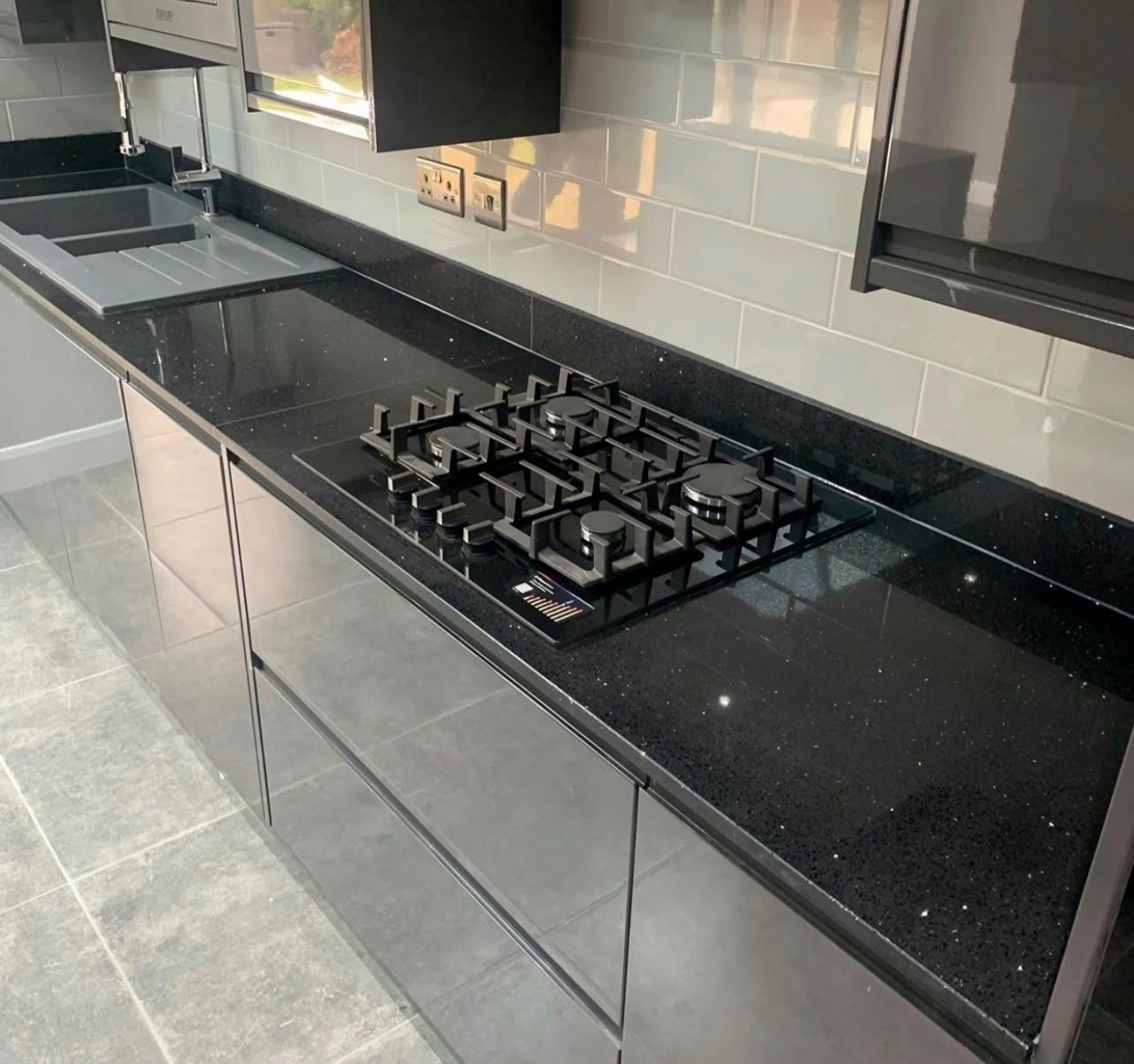 Gas hob in a Black Sparkle run below a metro tile splashback, with the sink and drainer beyond