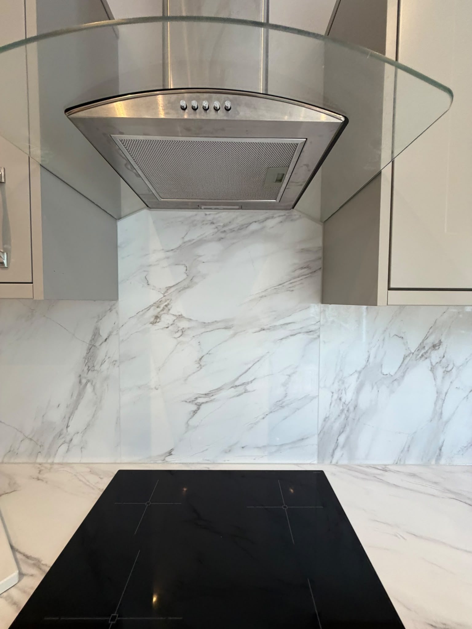 Calacatta Glacier splashback behind a black hob, running up to the chimney extractor