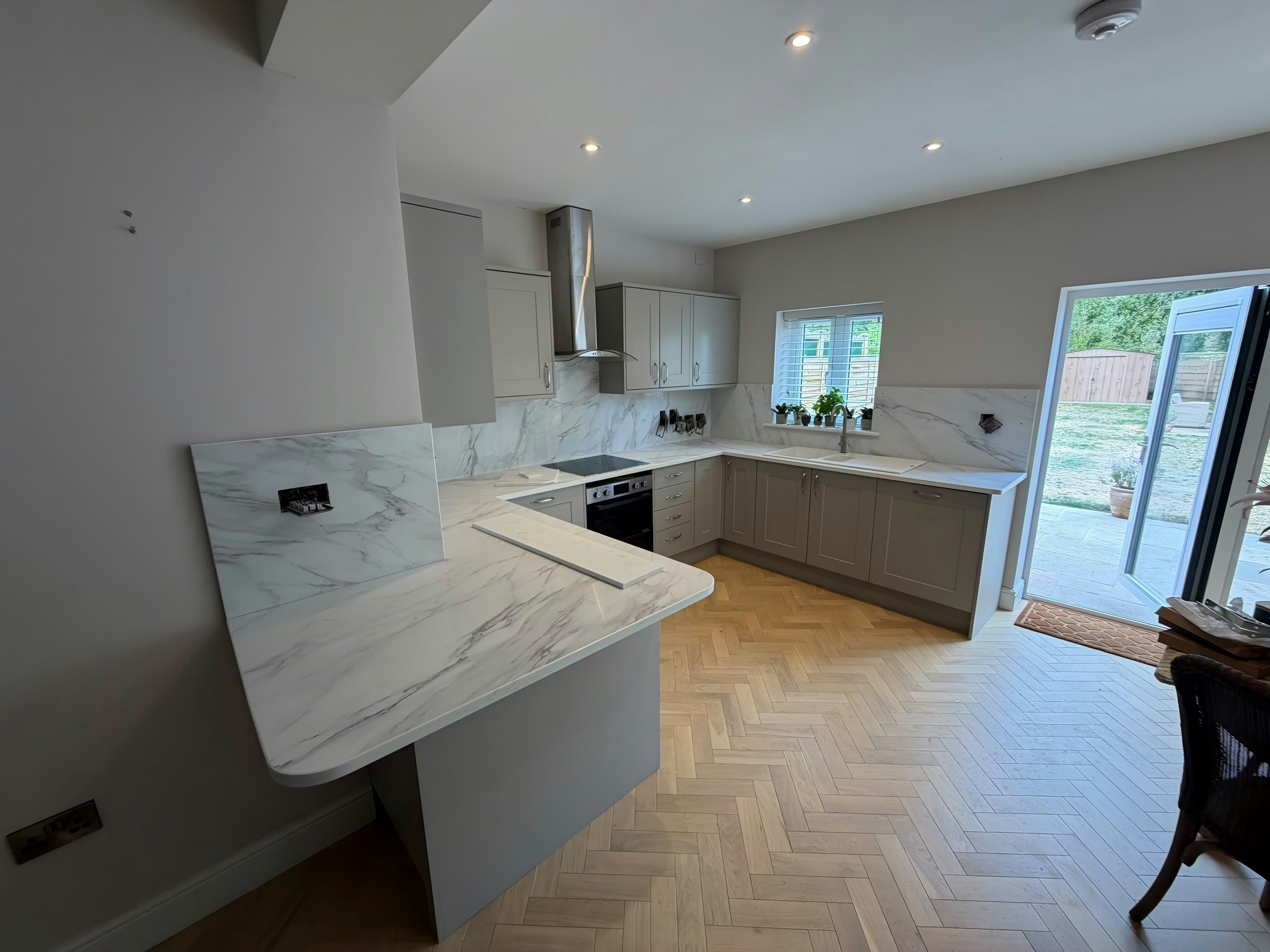 Calacatta Glacier worktops and matching splashback in a taupe shaker kitchen, with a curved peninsula end