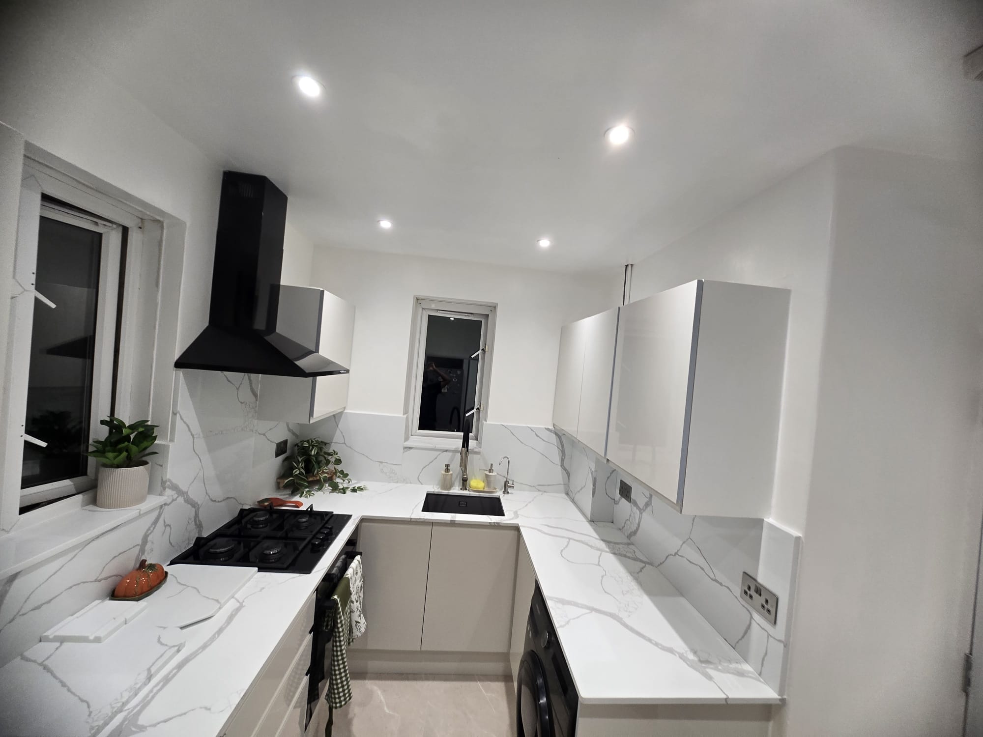 Calacatta Venato worktop and splashback past a black gas hob and chimney extractor to the undermount sink under the window