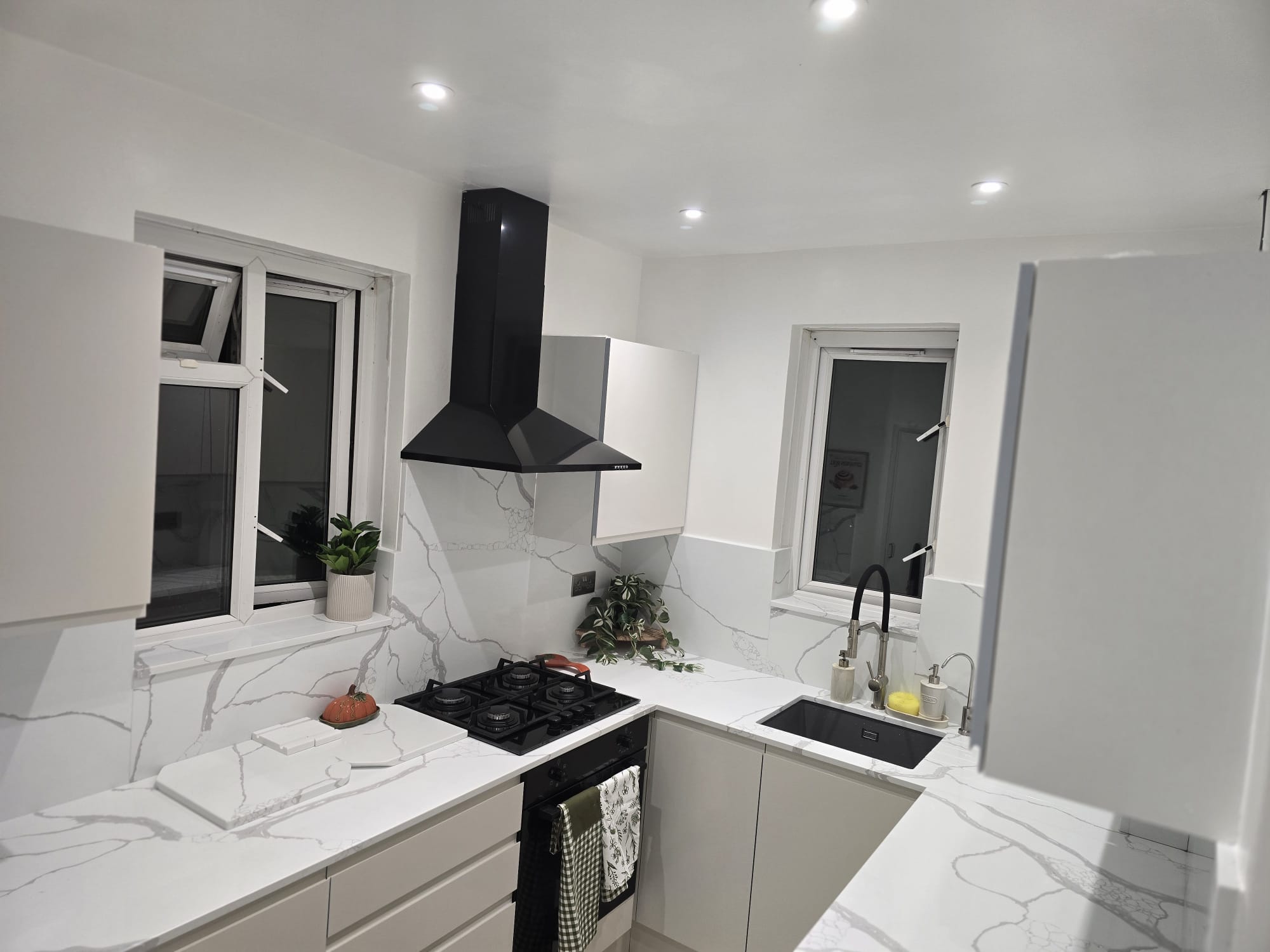 Close view of the Calacatta Venato splashback behind a black gas hob, soft grey veining against the stone grey doors