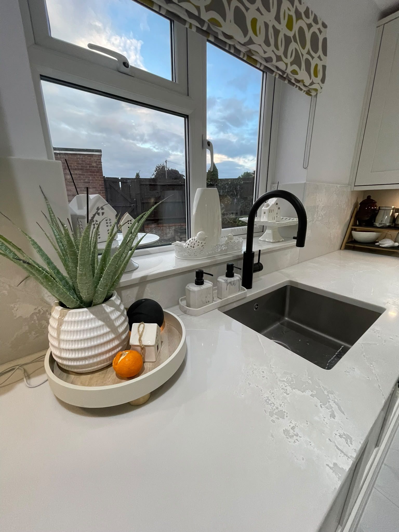 Polar White around the sink, with a plant and fruit on a tray beside the black tap