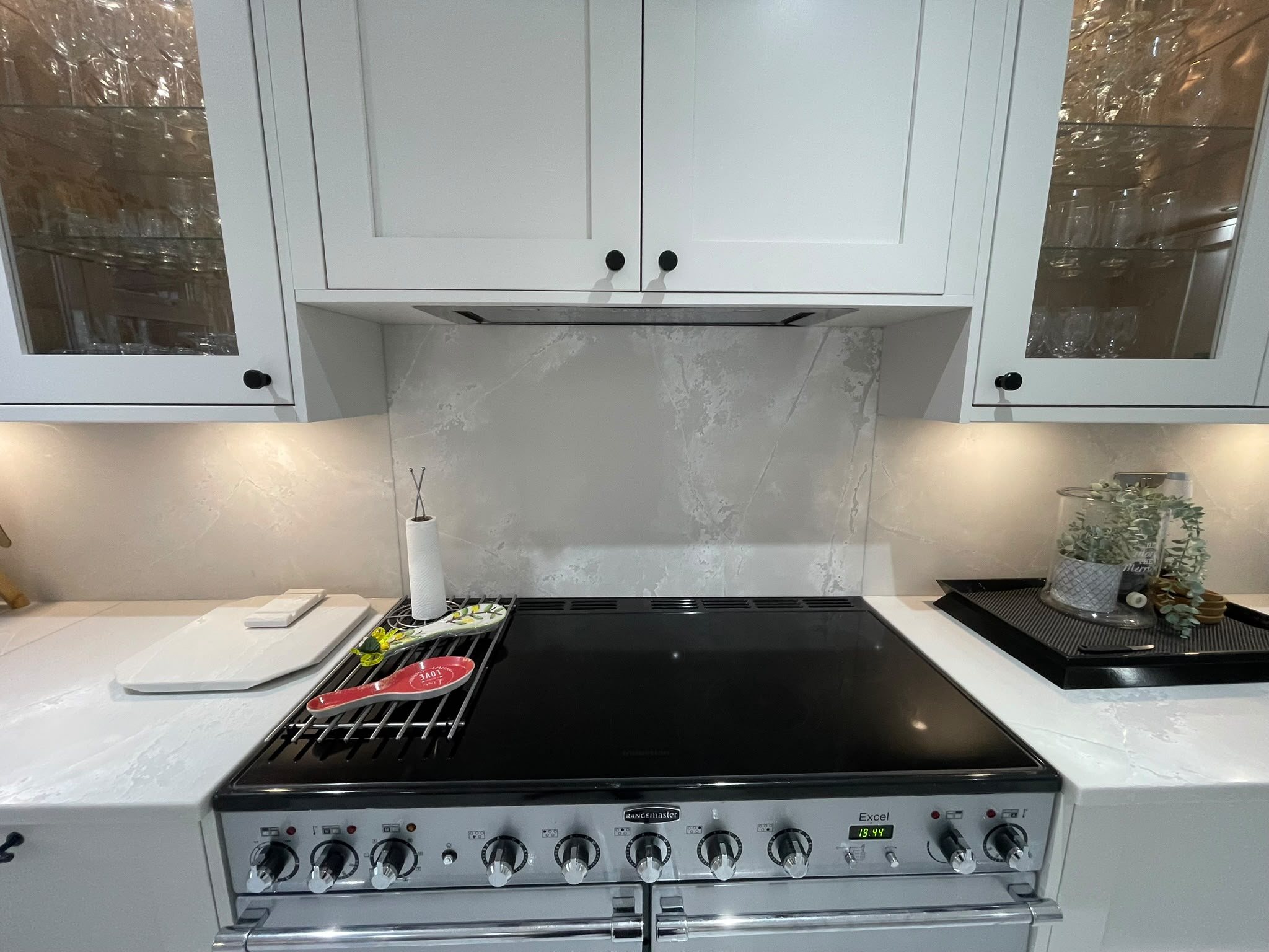 Range cooker set between Polar White runs, with a contrasting veined grey splashback carried up the wall behind it