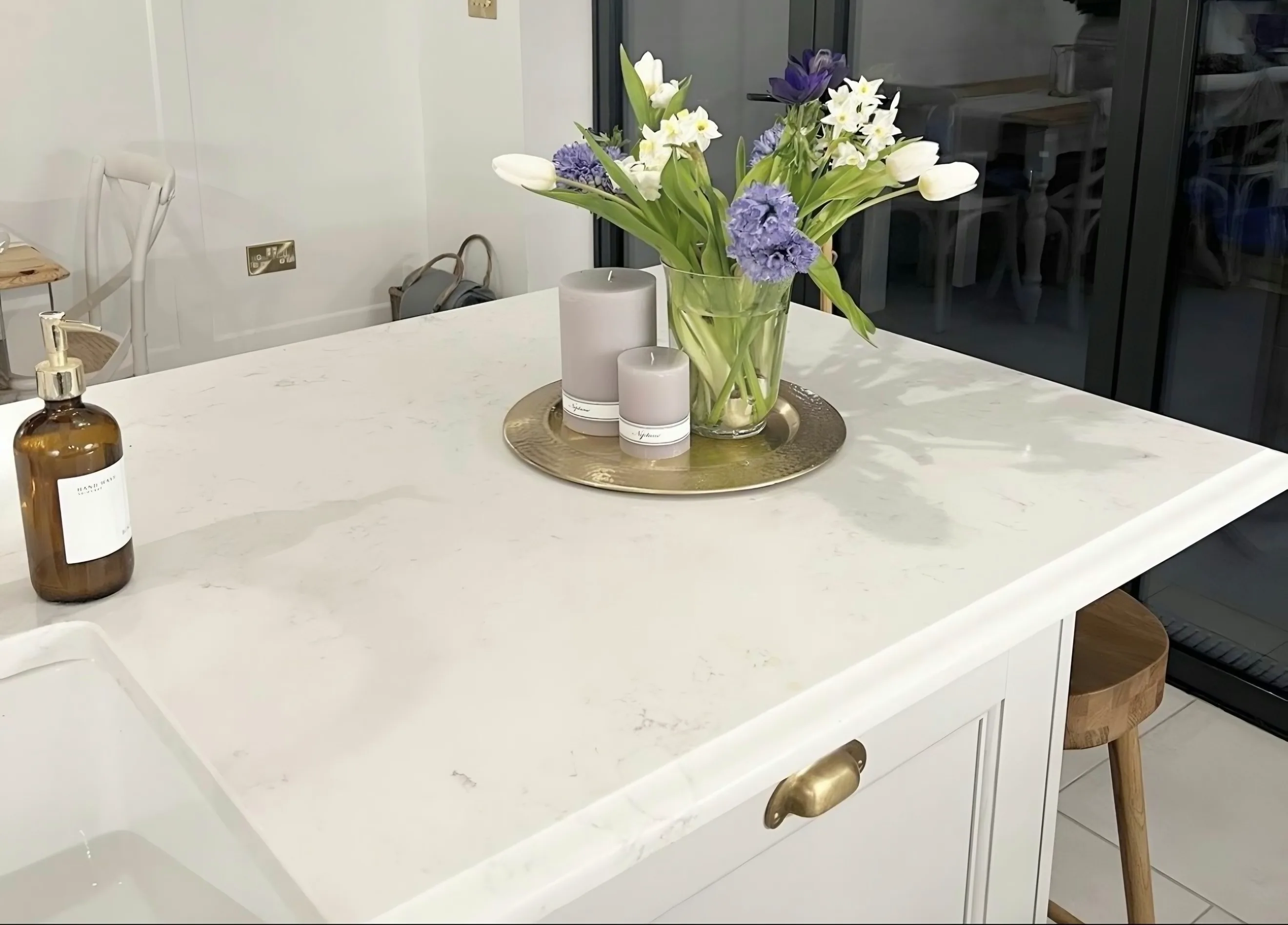 Capri White island beside the belfast sink, tulips on a brass tray and a wooden stool tucked under the overhang