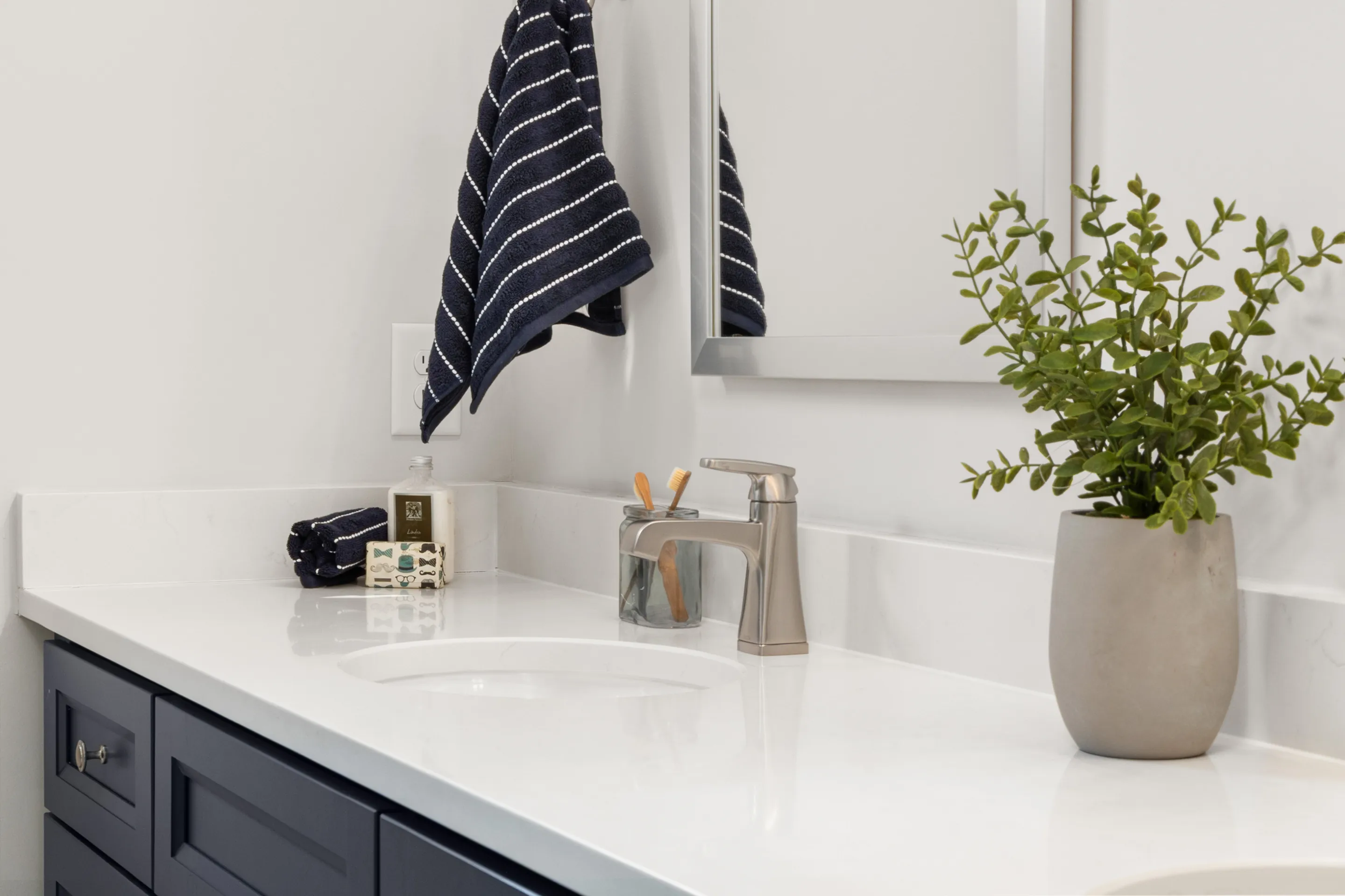 Bright modern bathroom vanity with a potted plant and striped towel.