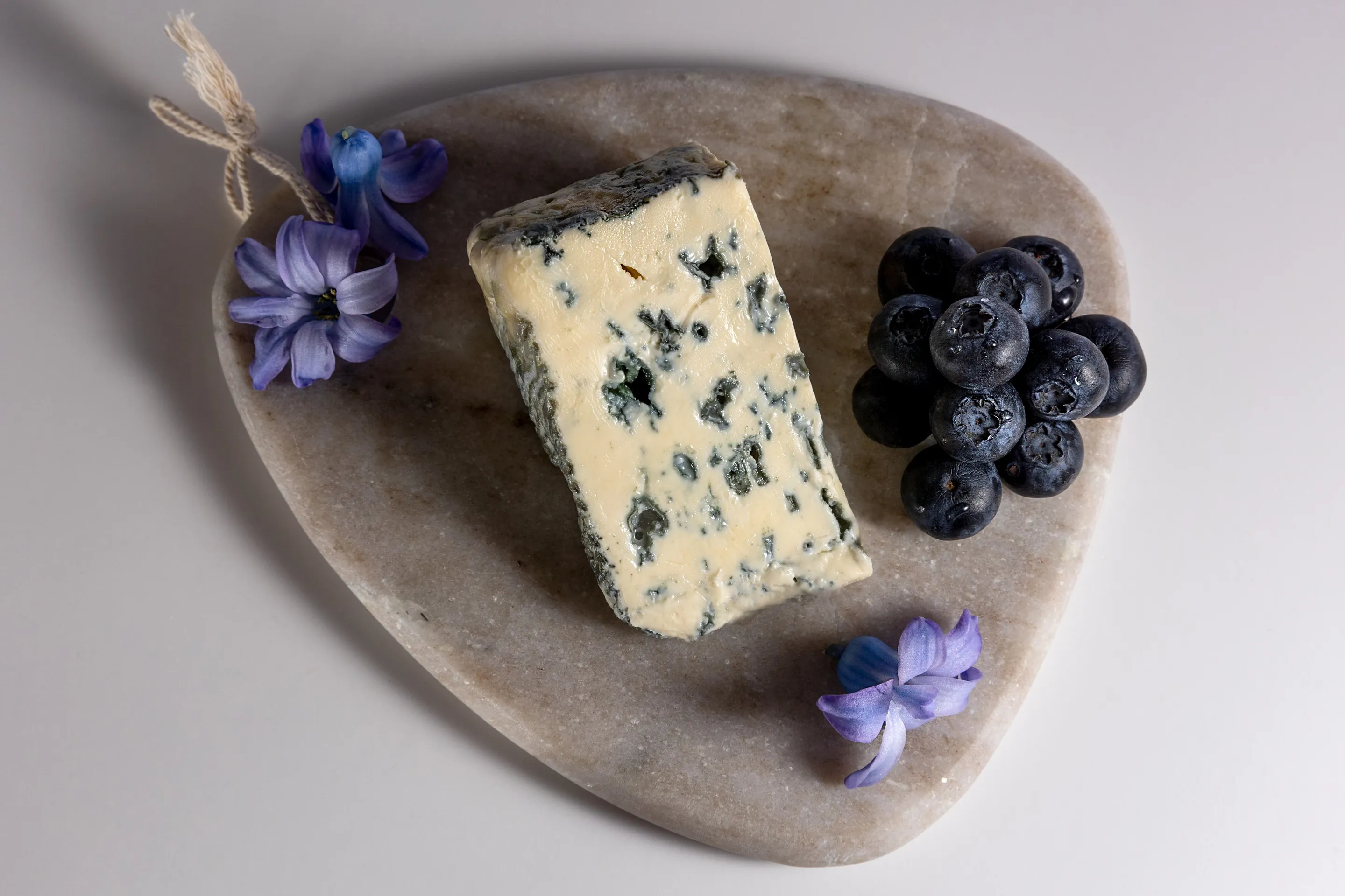 A wedge of blue cheese and black grapes on a rounded grey stone serving board