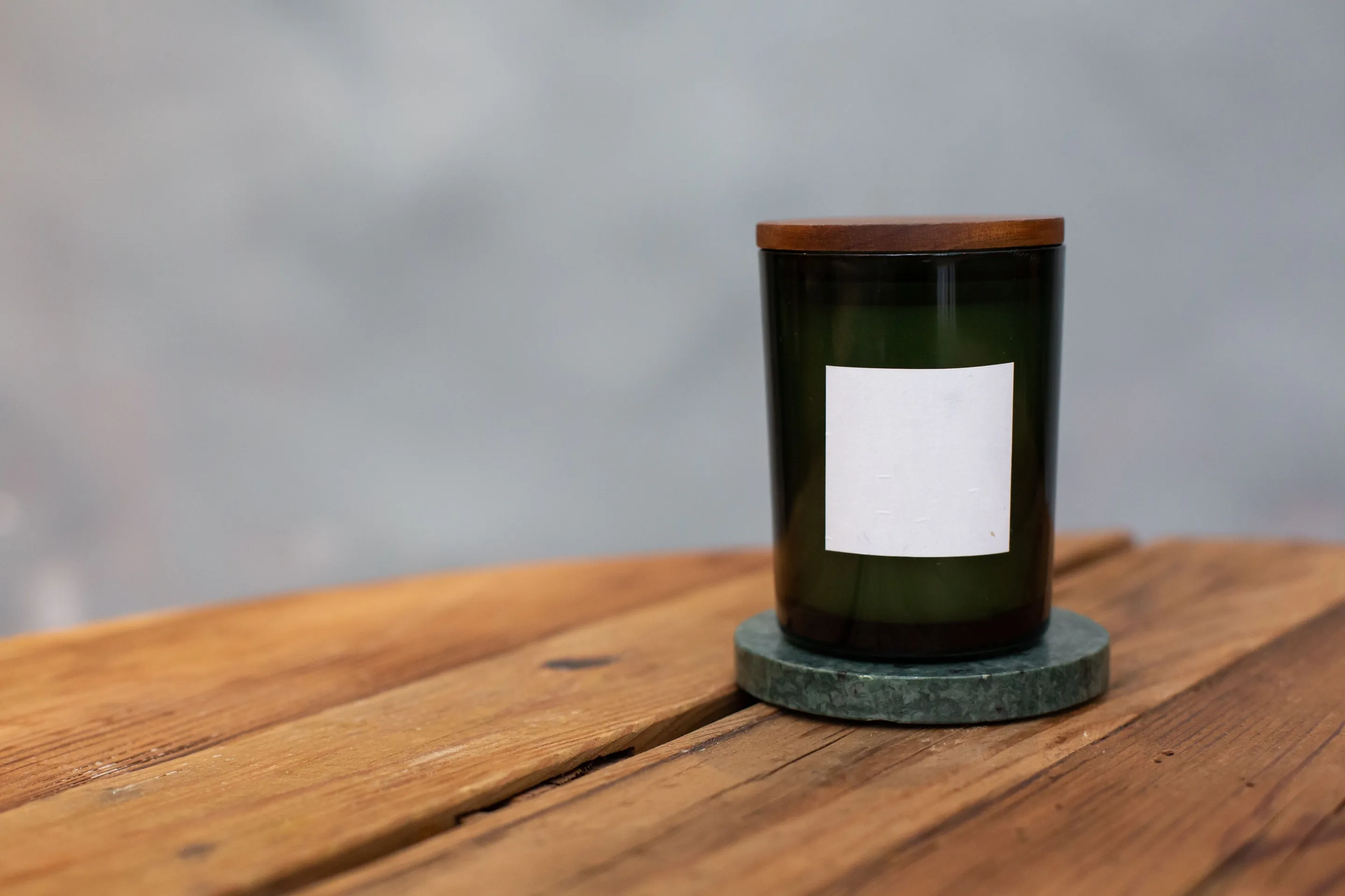 A candle in a green glass jar on a round green stone coaster on a weathered wooden table