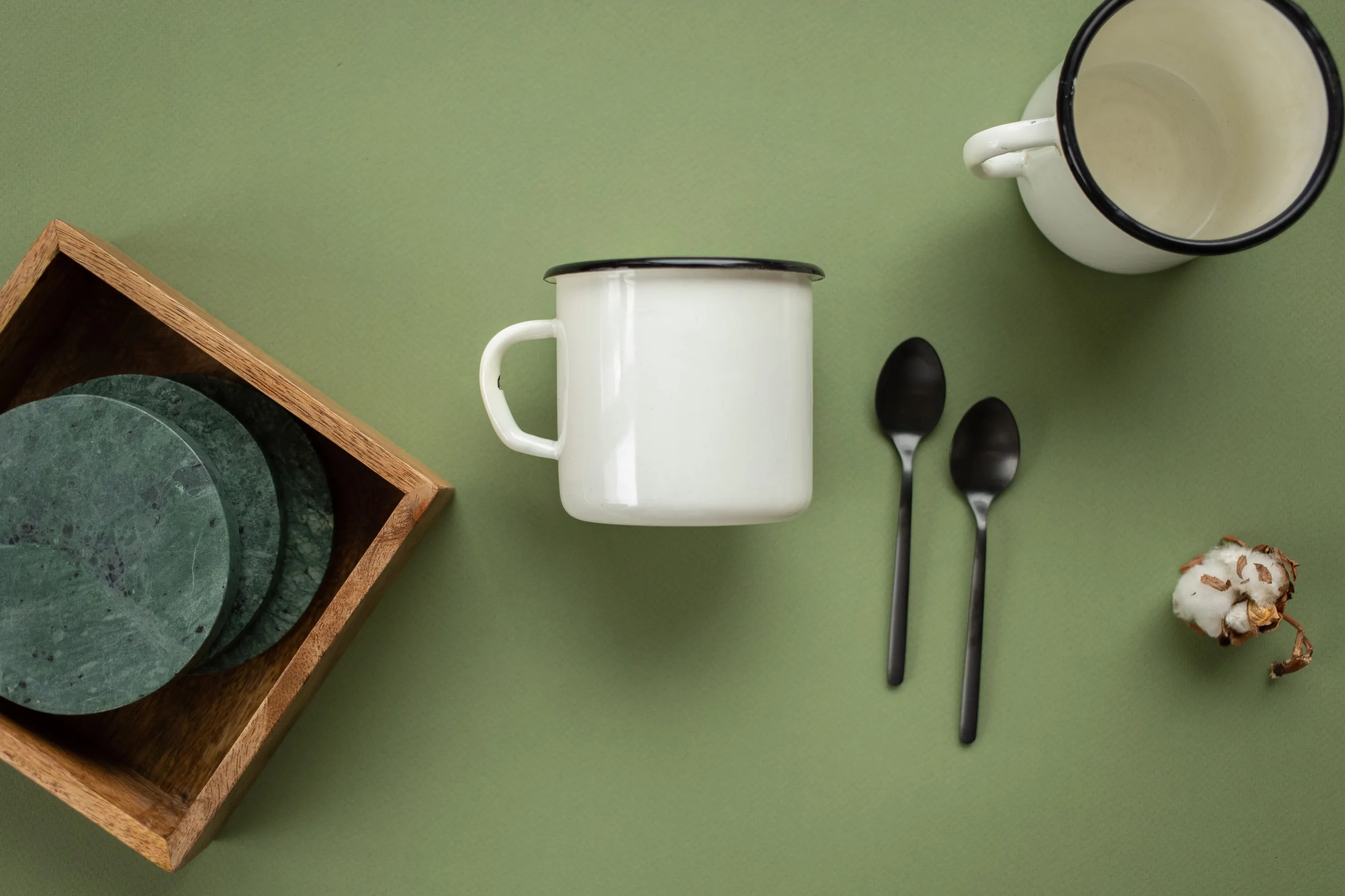 A set of round green stone coasters stacked in a wooden box beside an enamel mug