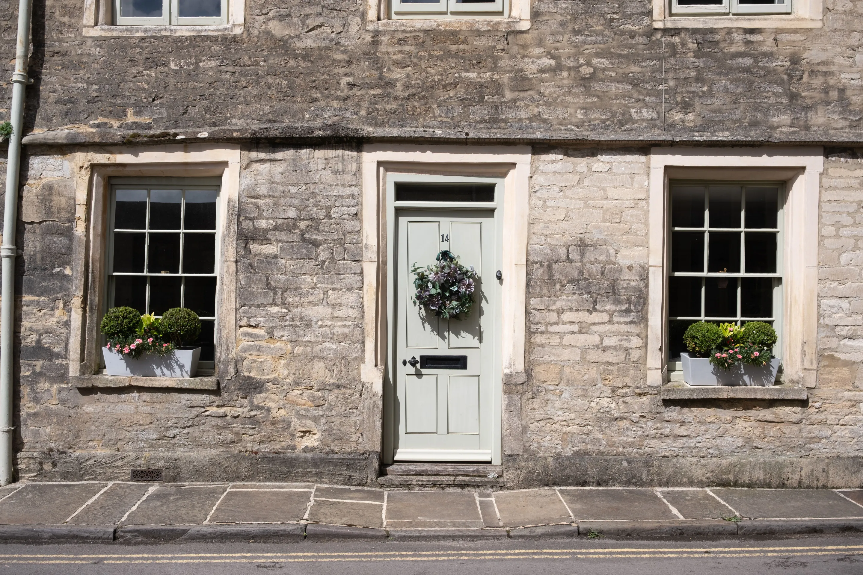 A limestone cottage front with a pale green door above a single stone doorstep at the pavement