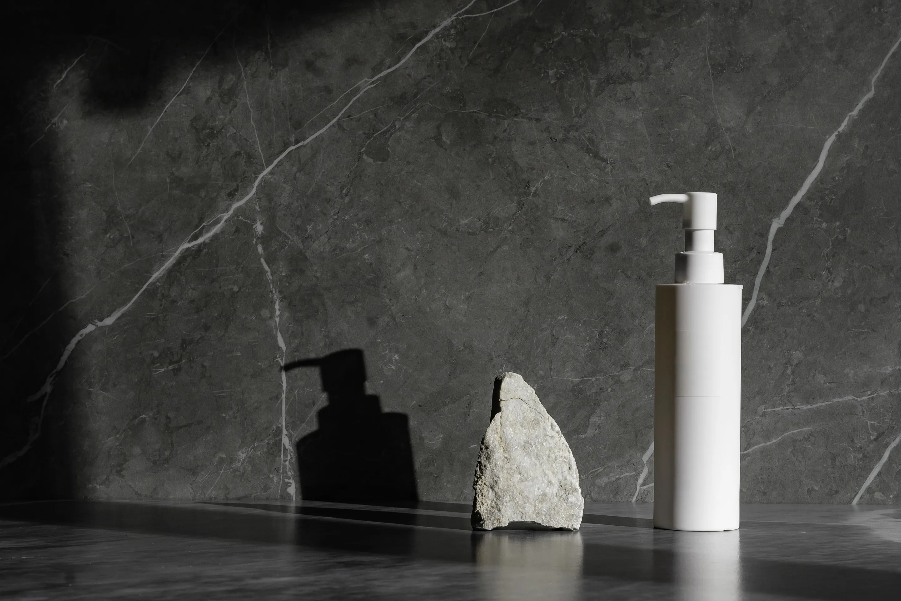 A white pump bottle and a small rock on a dark grey veined stone ledge