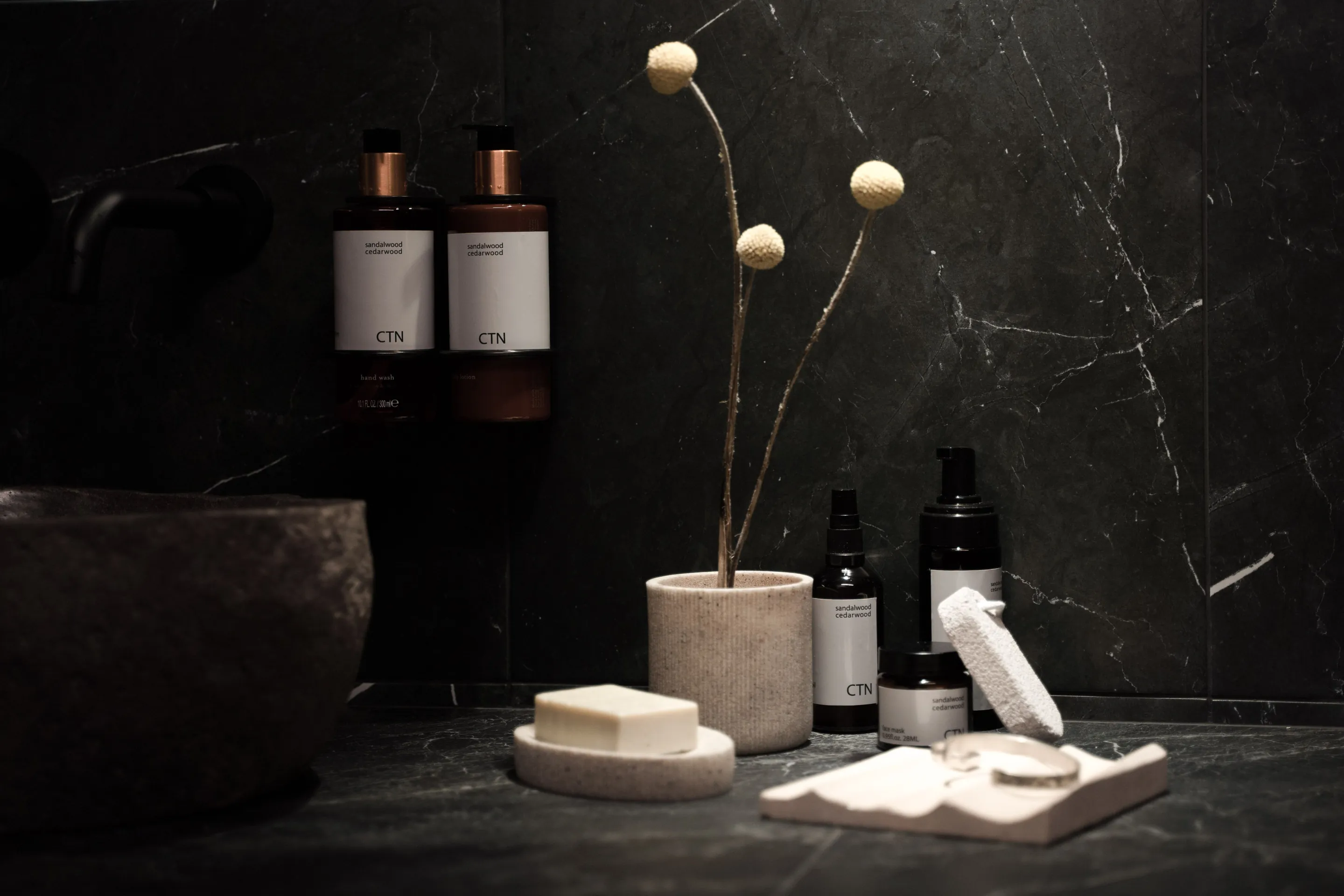 Toiletries and a soap dish on a black veined stone shelf against a matching wall