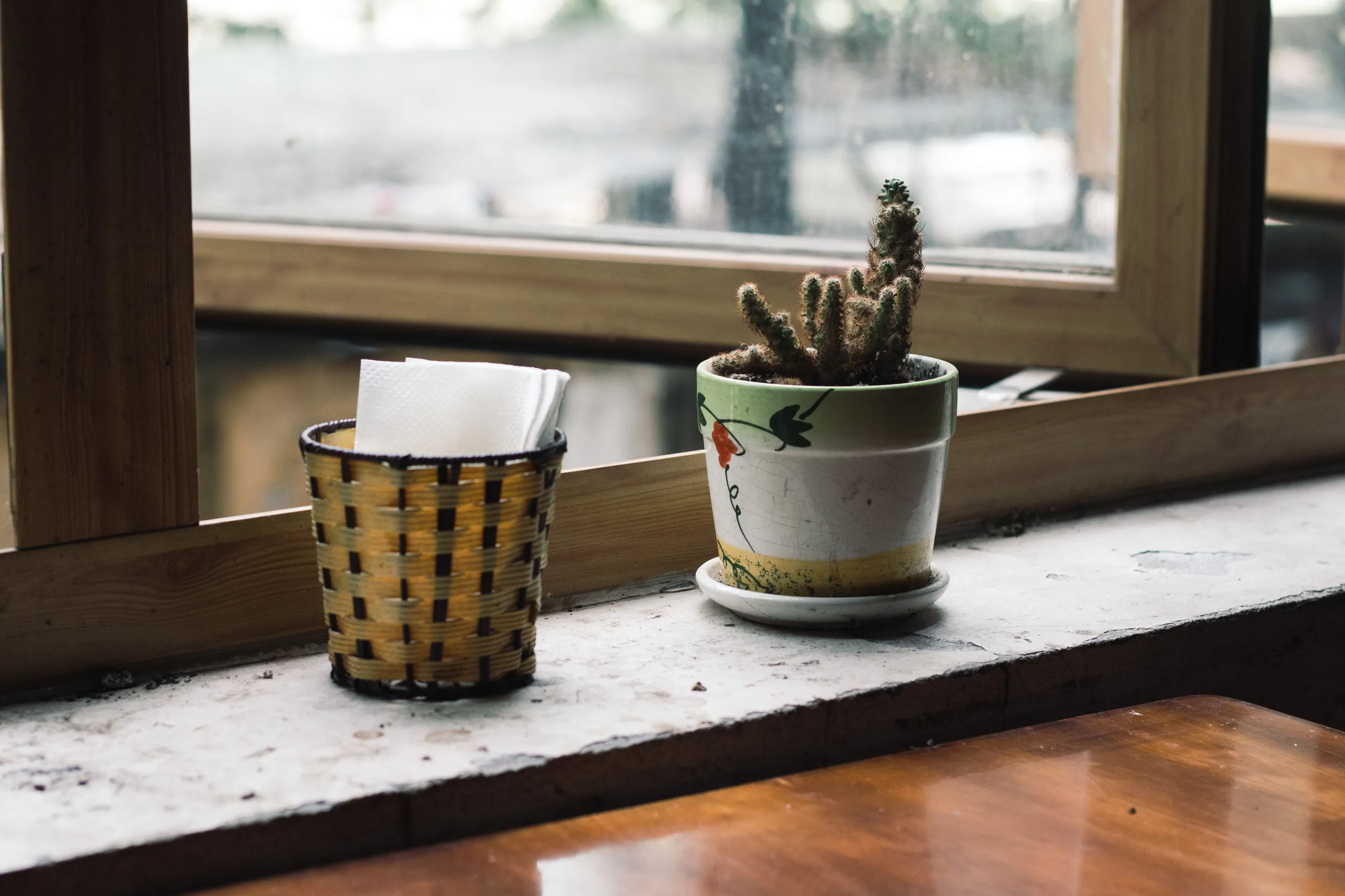 A pot plant and a napkin holder on a pale stone window sill behind a timber window frame