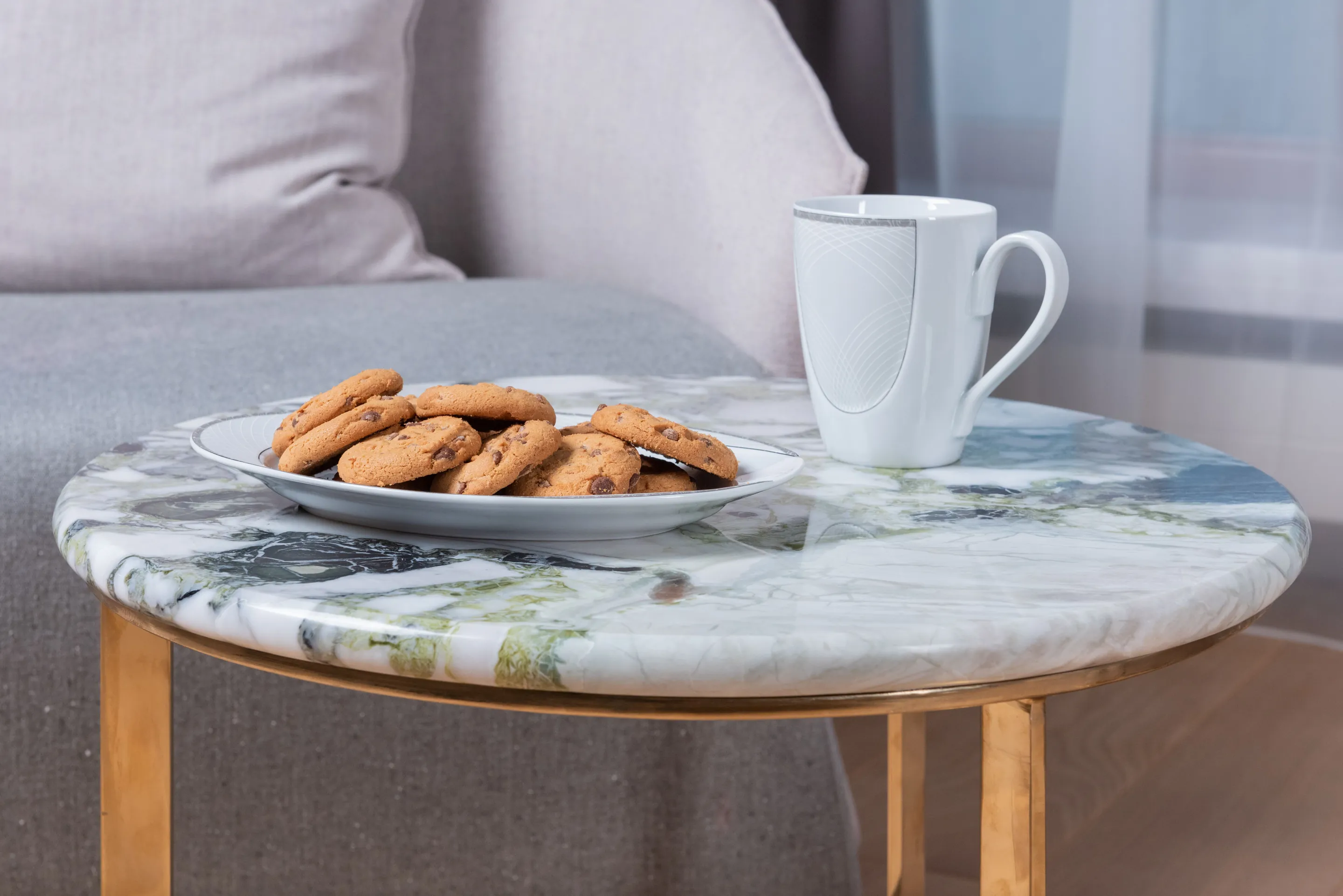 A round green and white veined stone side table top with a mug and a plate of biscuits